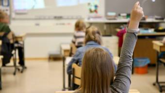 Skolelev i grå tröja räcker upp handen i ett klassrum.